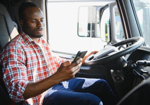 Young african american truck driver using mobile phone while driving transport vehicle